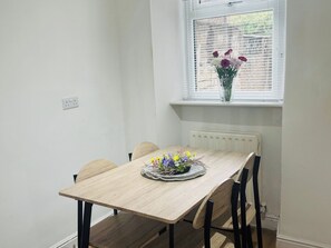Et spisebord med fire stole, en vase med blomster og et vindue med persienner.