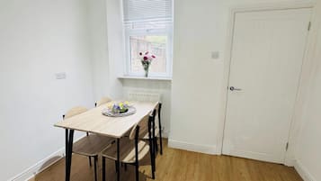Een eethoek met een houten tafel en stoelen, een raam met jaloezieën en een witte deur.