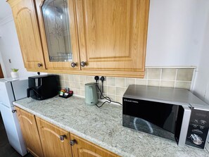 A kitchen with wooden cabinets, a microwave, a coffee maker, and a kettle.