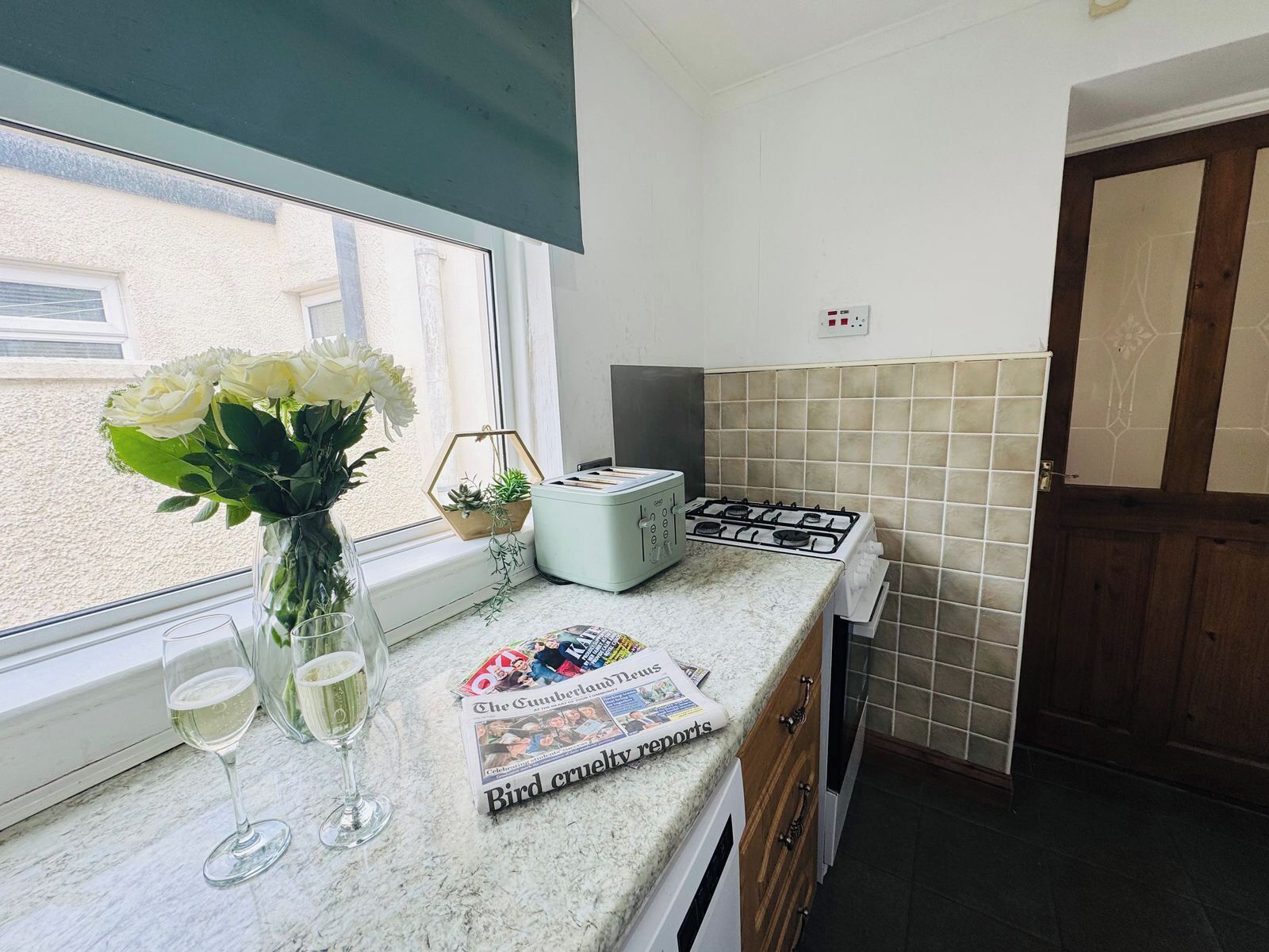 Eine Küche mit Fenster, Toaster, Zeitung und Blumen in einer Vase.