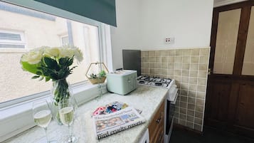 A kitchen with a window, a toaster, a newspaper, and a vase with flowers.