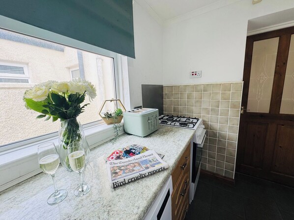 A kitchen with a window, a toaster, a newspaper, and a vase with flowers.