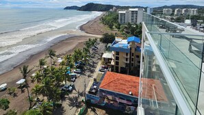 Vista costera con playa, palmeras y edificios con tejados rojos.