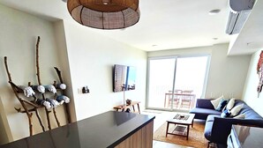 Una cocina moderna con una isla central, un rincón de comedor con sofá y mesa, y un amplio ventanal corredero al exterior.