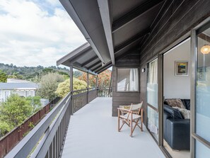 Un balcón con una silla de madera y un sofá, vistas a árboles y casas, y un cuadro en la pared.