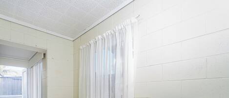 A small kitchen with a white refrigerator, a wooden table with chairs, and a window with white curtains.
