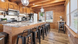 Una cocina con armarios de madera, encimera de granito, microondas de acero inoxidable y una barra con taburetes.