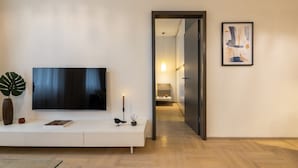 Un salon moderne avec un téléviseur à écran plat posé sur une console blanche, une plante en pot, une bougie et un tableau abstrait encadré accroché au mur.