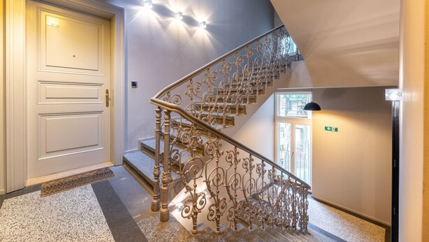 Un escalier orné de rampes en métal ouvragé, une porte blanche et une enseigne lumineuse fixée au mur.