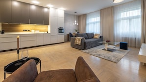 Un salon moderne avec un canapé gris, une table basse en verre et un coin repas comprenant une table et des chaises blanches.