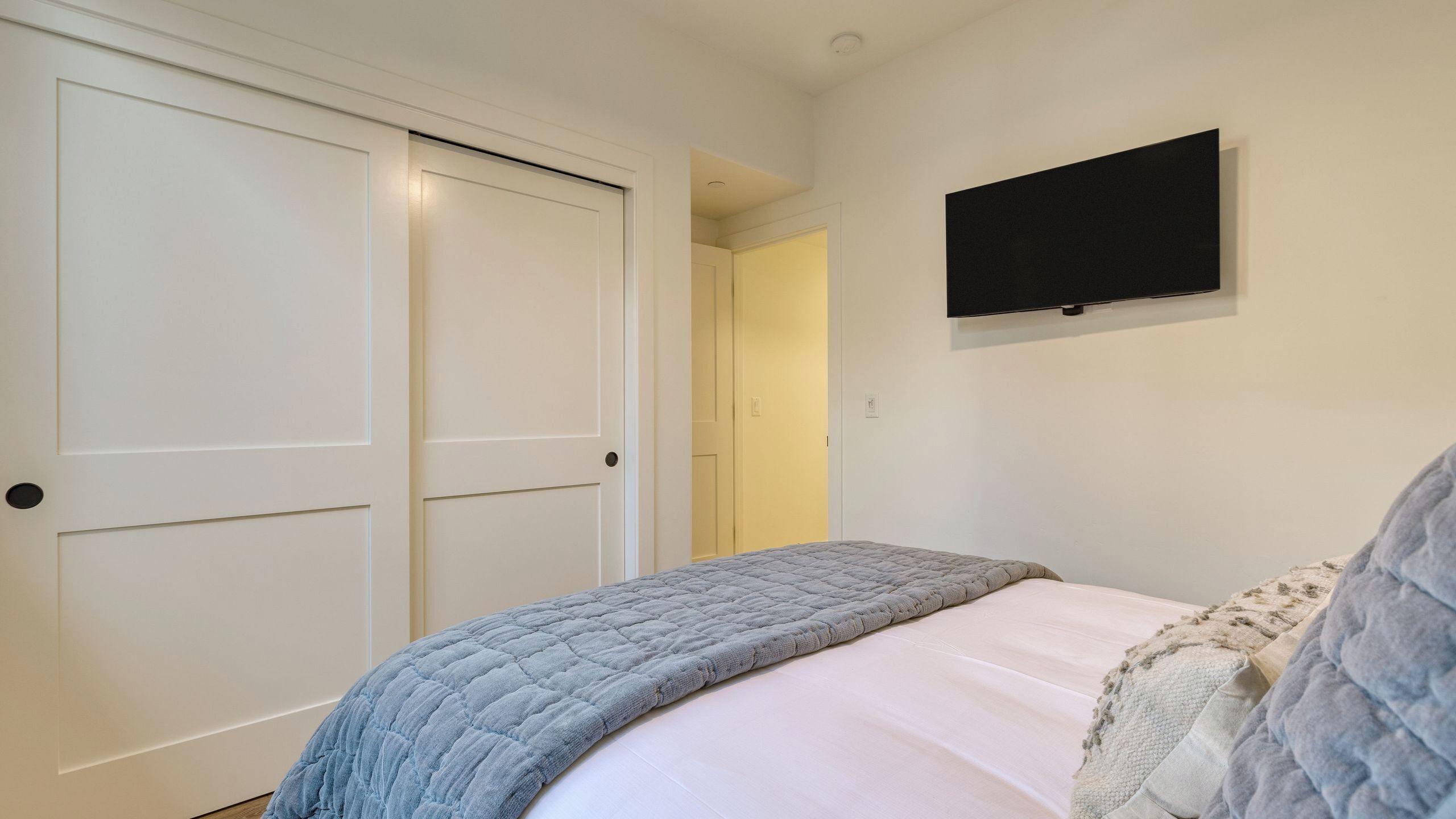 A bedroom with a bed, a television mounted on the wall, and a door leading to another room.