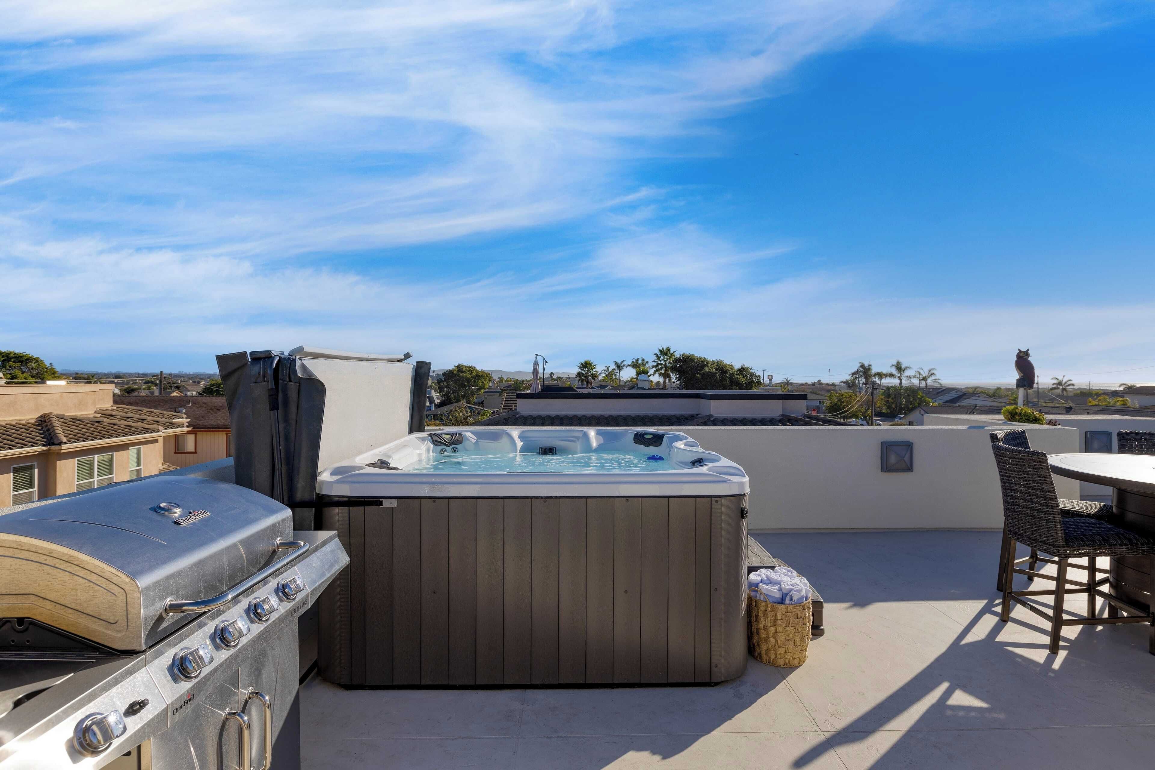 A rooftop patio with a hot tub, a grill, and outdoor seating.