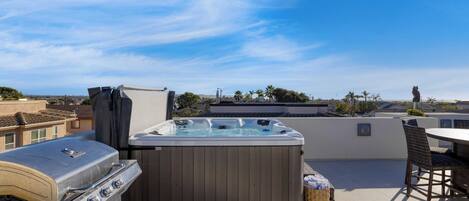 A rooftop patio with a hot tub, a grill, and outdoor seating.