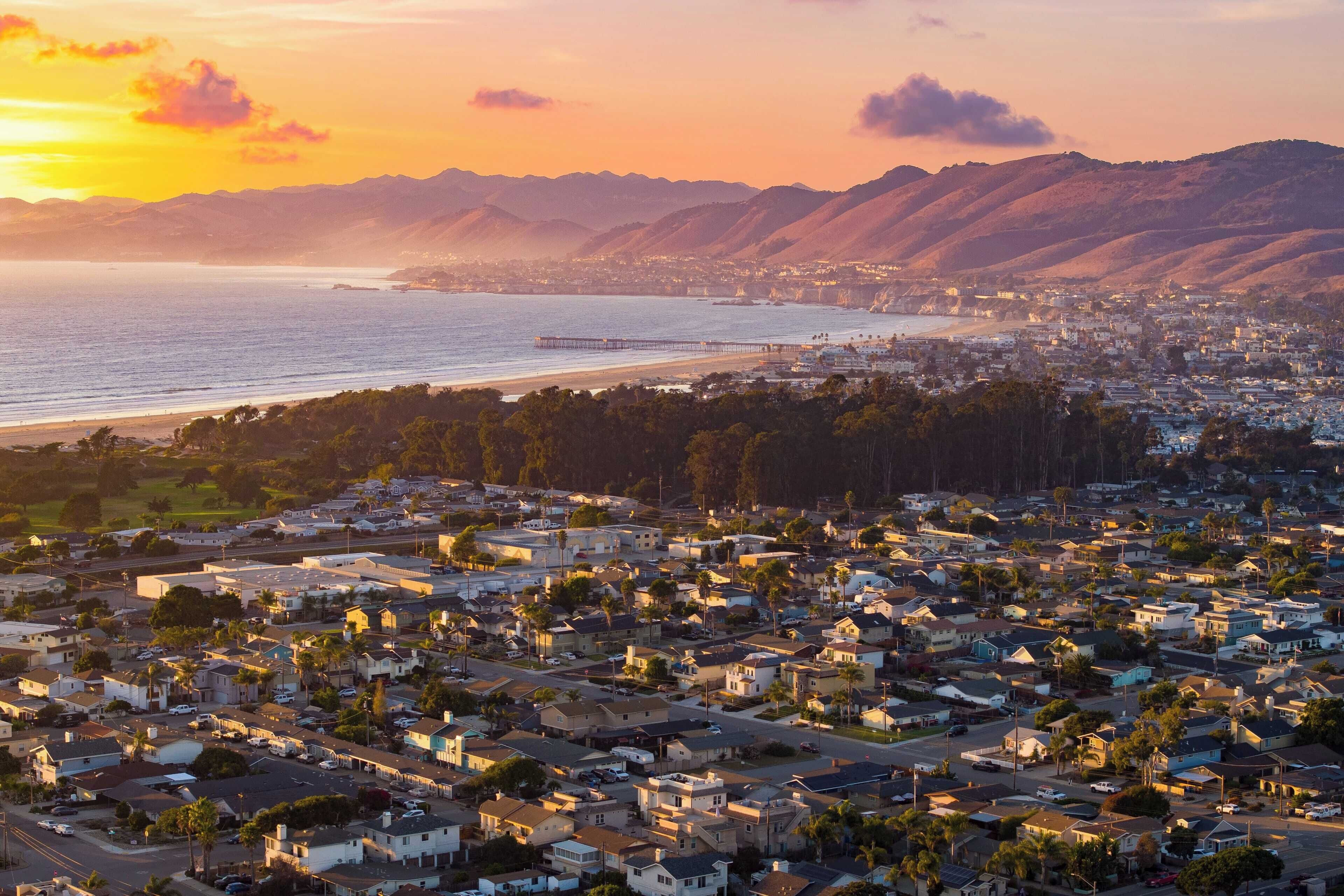 A coastal residential area with houses, a pier, and mountains in the background.