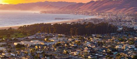 A coastal residential area with houses, a pier, and mountains in the background.