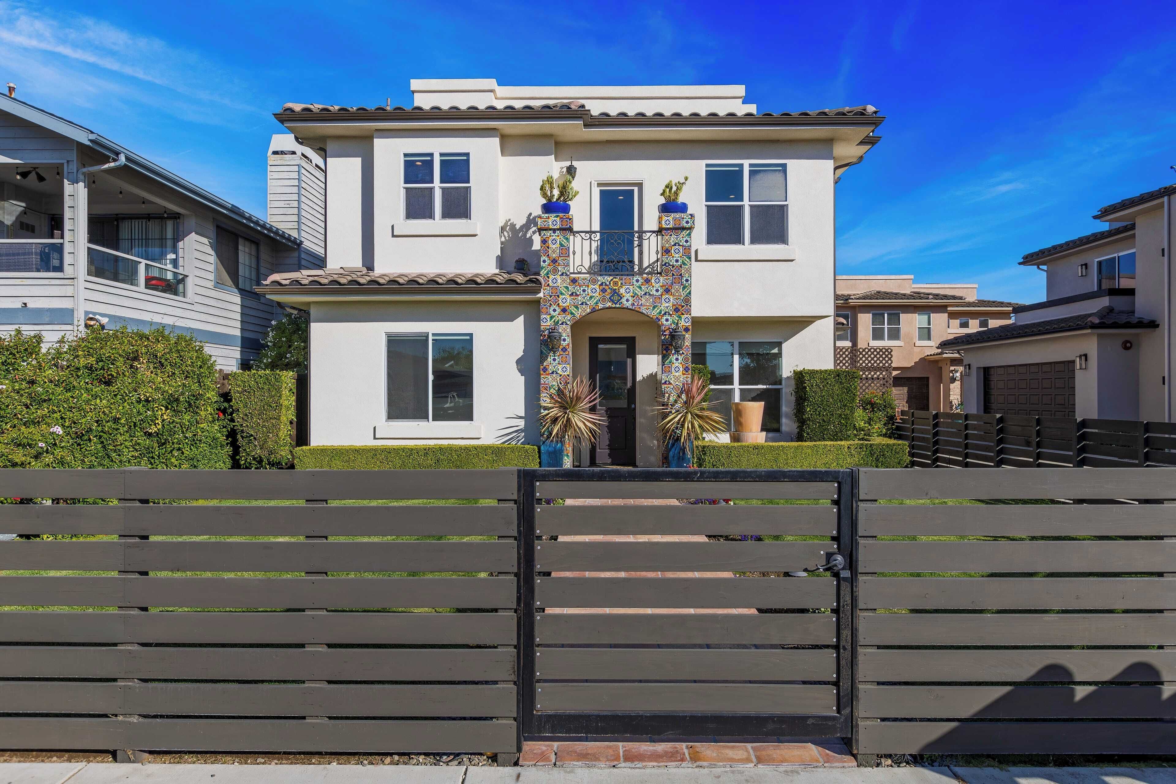 A two-story house with a decorative entrance, a gated driveway, and a well-maintained lawn.