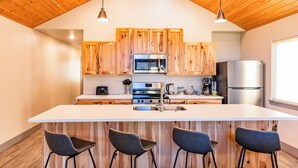 Une cuisine moderne avec des meubles en bois, un îlot central doté de tabourets, des appareils en acier inoxydable et un éclairage suspendu.
