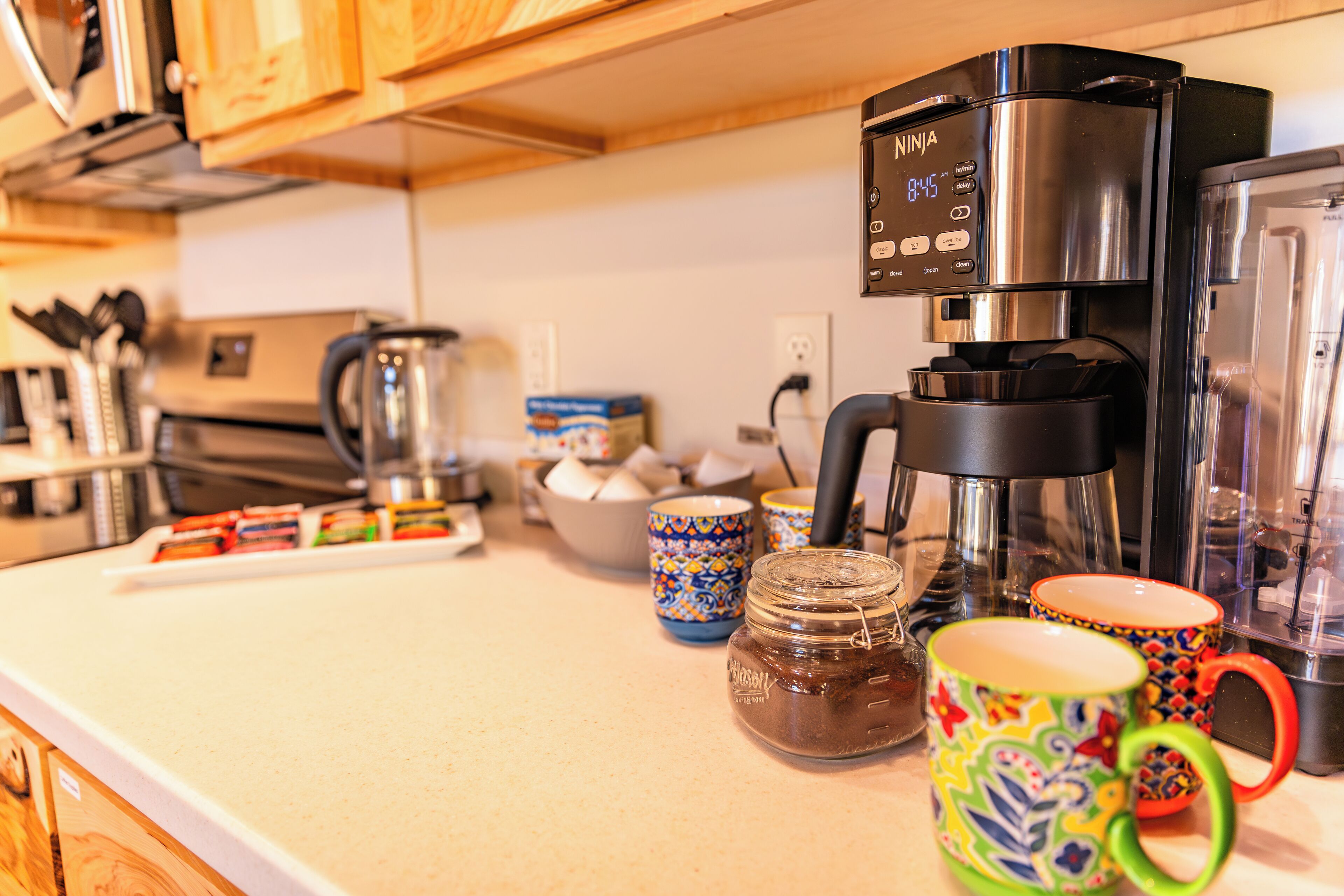 A kitchen with a coffee maker, jars, and colorful mugs on the counter.