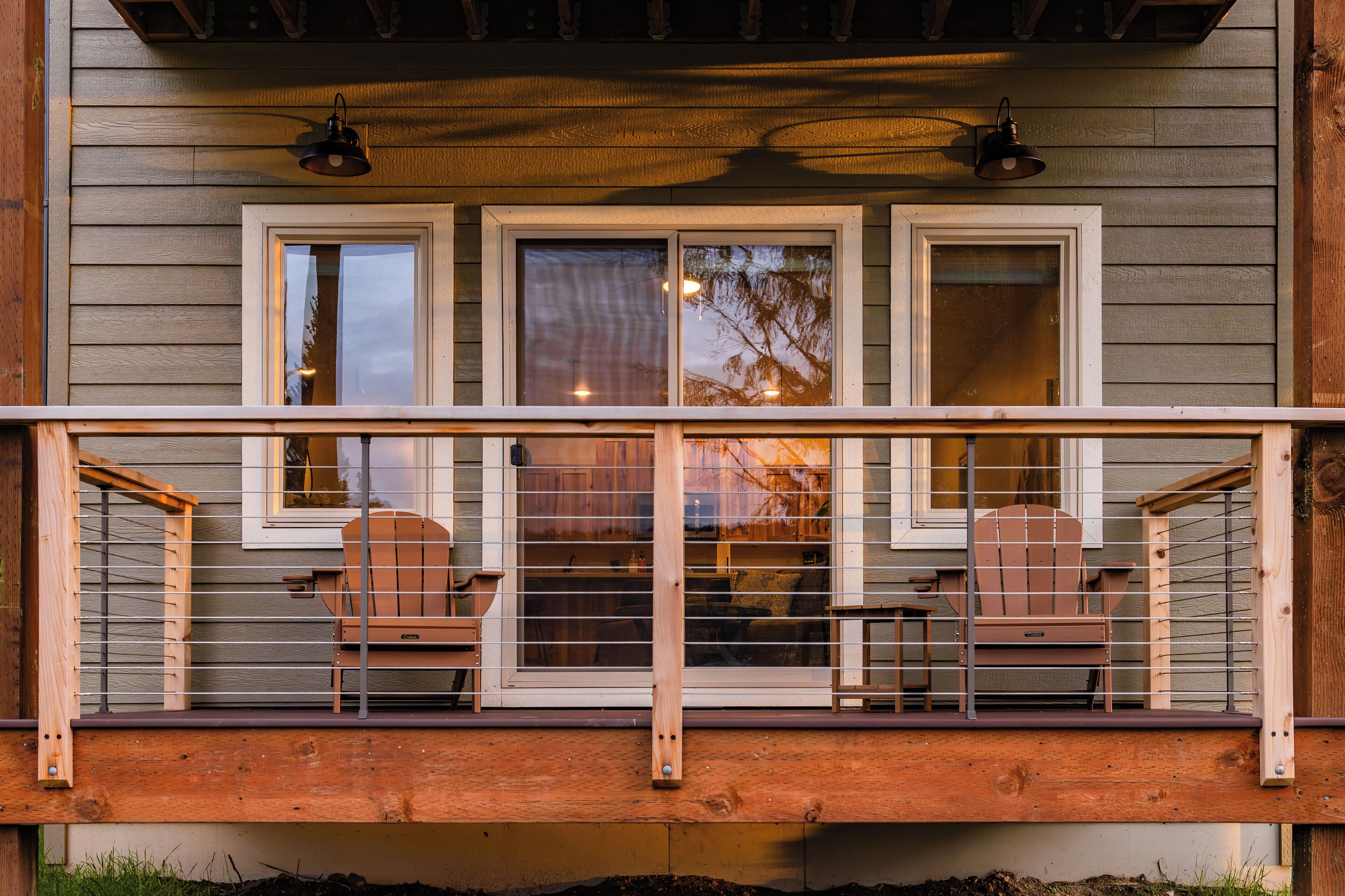 A wooden deck with two Adirondack chairs and a railing.