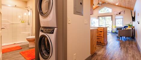 A laundry area with a washing machine and dryer, a shower, and a wooden floor.