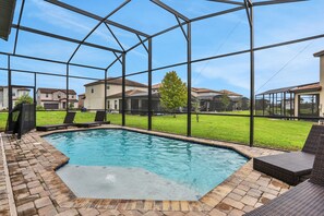 A swimming pool with a glass enclosure, surrounded by lounge chairs and a brick patio.