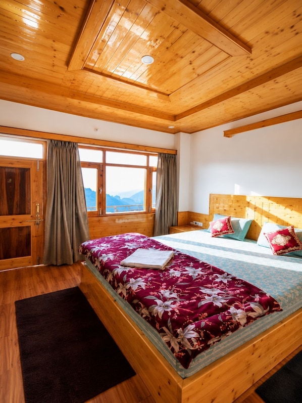 A wooden room with a bed, curtains, and a window with a mountain view.