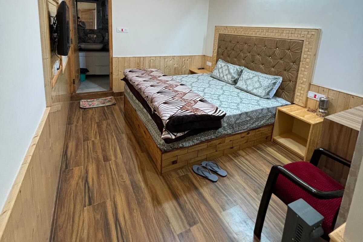 Une chambre avec un plancher en bois, un lit avec une literie à motifs, une tête de lit, une table de chevet, une chaise rouge et un luminaire au plafond.