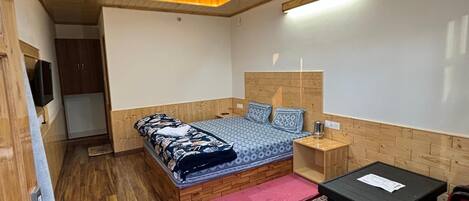 Un dormitorio pequeño con techo de madera, cama con ropa de cama estampada, una mesita y una silla roja.
