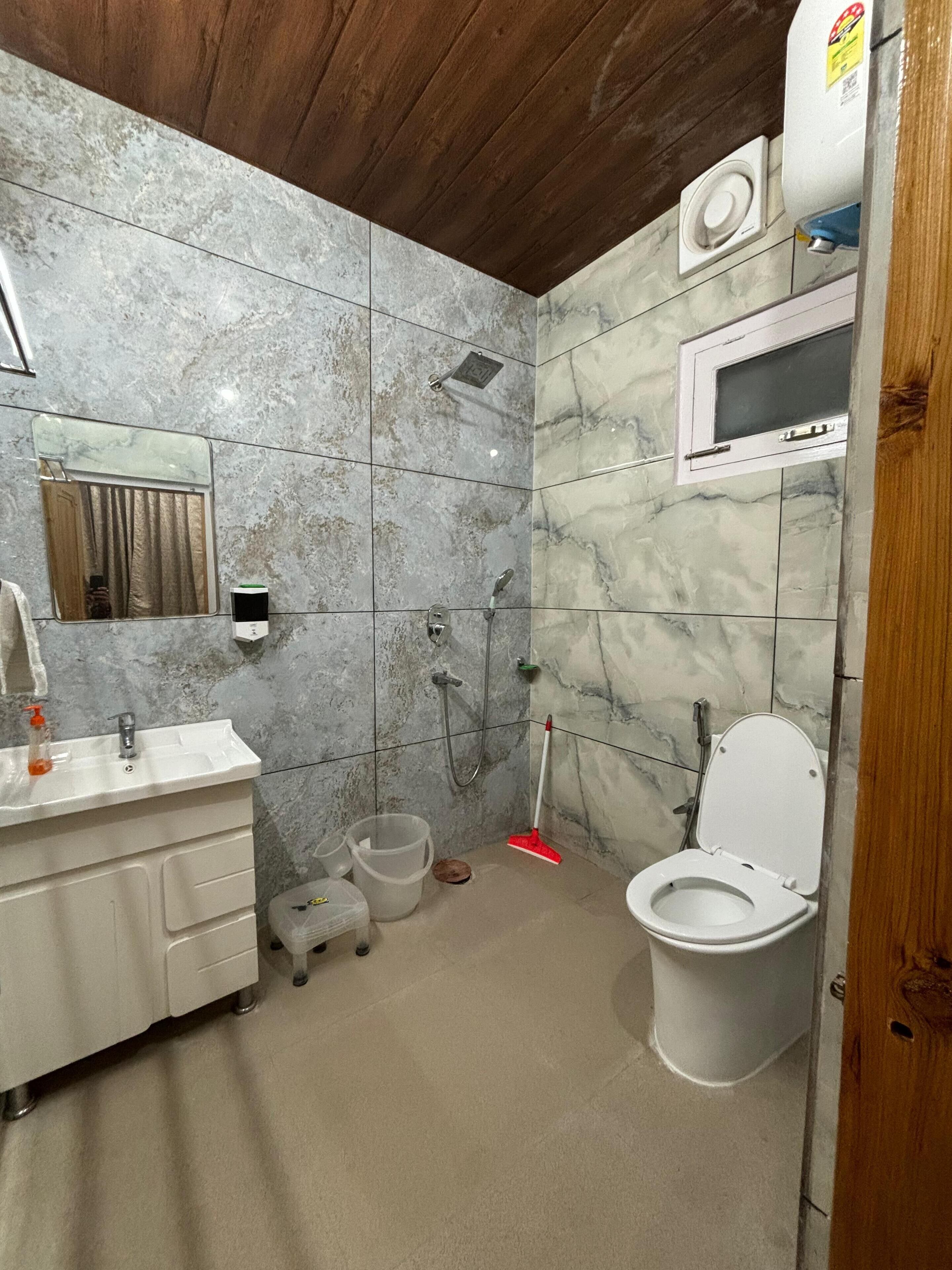 Un baño con pared de mármol, un lavabo, un inodoro, una ducha y un espejo.