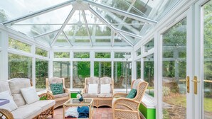 Une véranda meublée de mobilier en osier, dotée d’un toit en verre et offrant une vue sur le jardin.