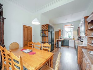 A dining area with a wooden table and chairs, a bookshelf, and a kitchen in the background. - 6 bedroom accommodation in Cardross, near Dumbarton (Cardross, near Dumbarton)
