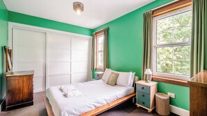 Une chambre à coucher avec un lit, une table de chevet, une lampe et une fenêtre avec des rideaux.