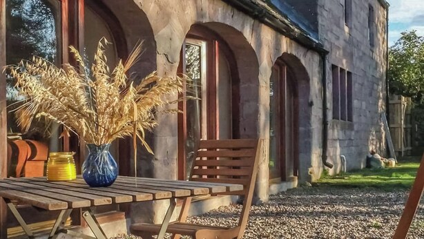A rustic building with arched windows and a wooden table with chairs outside. - 2 bedroom accommodation in Forfar (Forfar)