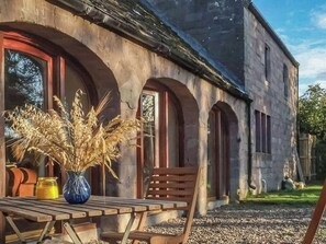 A rustic building with arched windows and a wooden table with chairs outside. - 2 bedroom accommodation in Forfar (Forfar)