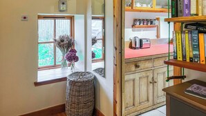 A room with a wooden cabinet, a wicker basket, a window with a view of greenery, and a bookshelf with books. - 2 bedroom accommodation in Forfar (Forfar)