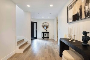 A hallway with wooden flooring, a staircase, a black console table with candles, a bust sculpture, and a round mirror on the wall. - Central Mini putt getaway (San Jose)