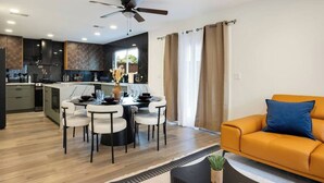 A modern kitchen with a dining area, a ceiling fan, and a living room with an orange sofa.