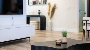 A modern living room with a white sofa, a curved coffee table with a plant, and a fireplace with decorative items.