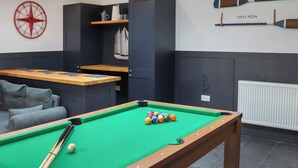 Ein Billardtisch mit Kugeln, eine Uhr und eine Wand mit zwei Paddleboards.