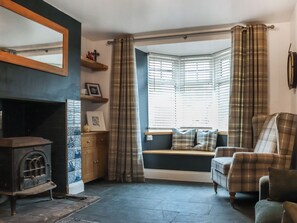 A cozy living room with a fireplace, a bay window with curtains, a sofa, and a wooden cabinet.