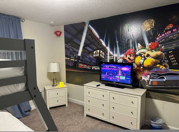 Une chambre avec un lit superposé, un téléviseur posé sur une commode et une fresque murale sur le thème de Mario.