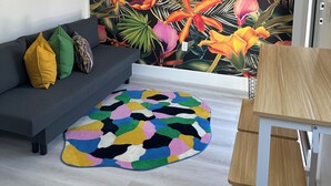 A modern living room with a gray sofa, colorful pillows, a vibrant tropical mural, and a wooden dining table. - Charming 1-bedroom apartment with AC, WiFi in Heart of Miami (Miami)