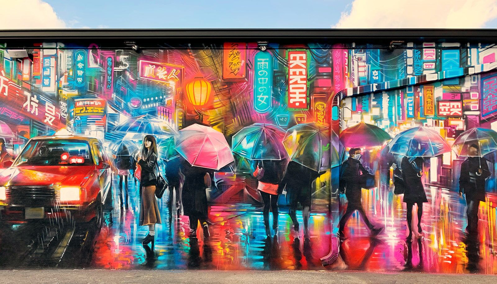 A vibrant mural with figures holding umbrellas, a red car, and neon signs on a building facade.