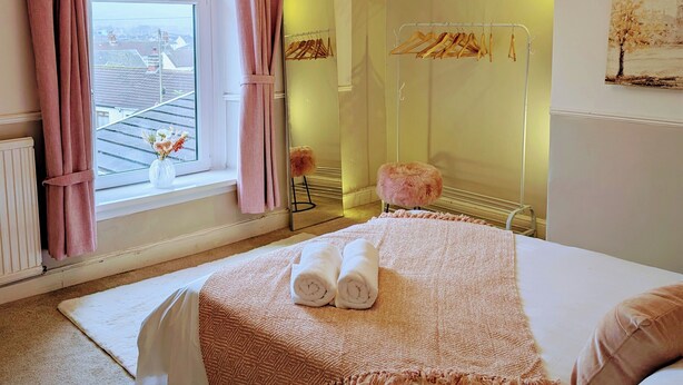 A bedroom with a large bed, a window with curtains, a hanging light fixture, and a radiator. - Ty Hiraeth 

A Charming Stay Steps Away from Caerphilly Castle!
 (Caerphilly)
