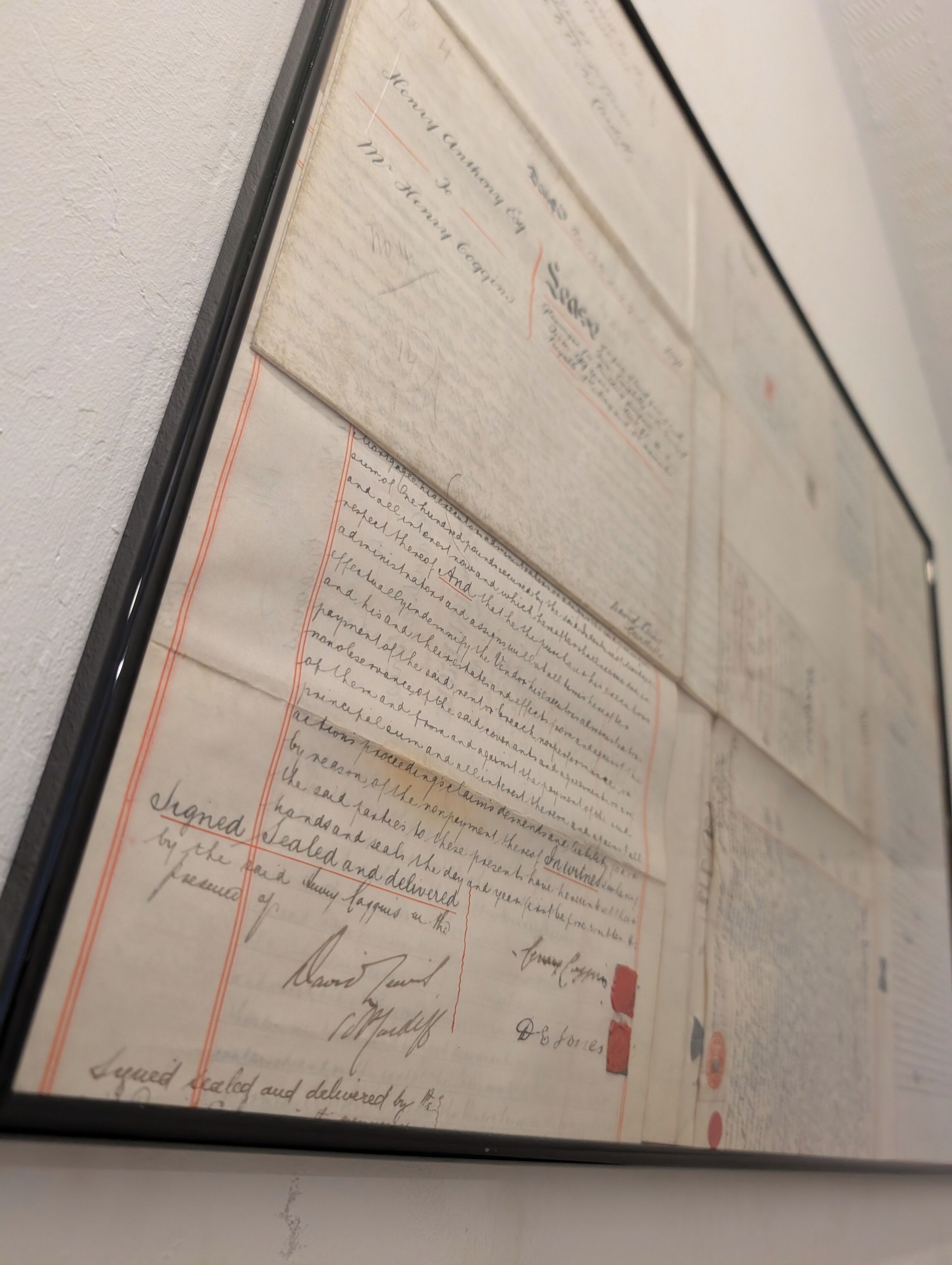 A framed document with handwritten text and red lines, possibly a historical record or official document.