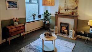 A cozy living room with a fireplace, a large window, a wooden bench, a round table, and a hanging light fixture. - Ty Hiraeth 

A Charming Stay Steps Away from Caerphilly Castle!
 (Caerphilly)