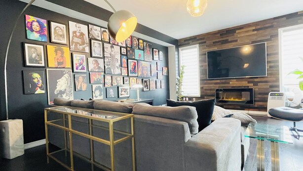 Uma sala de estar moderna com um sofá cinza, uma mesa de centro de vidro e uma parede decorada com obras de arte emolduradas.