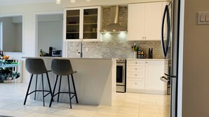 Cozinha moderna com armários brancos, uma ilha central com banquetas, geladeira de aço inoxidável e painel de parede de tijolos.