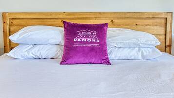 Uma cama com lençóis brancos, um travesseiro roxo com um logotipo e um cobertor estampado em tons de verde-água.