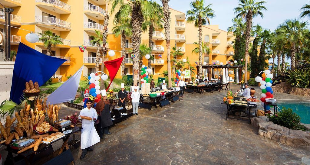 An outdoor dining area with food stalls, palm trees, and a pool.
